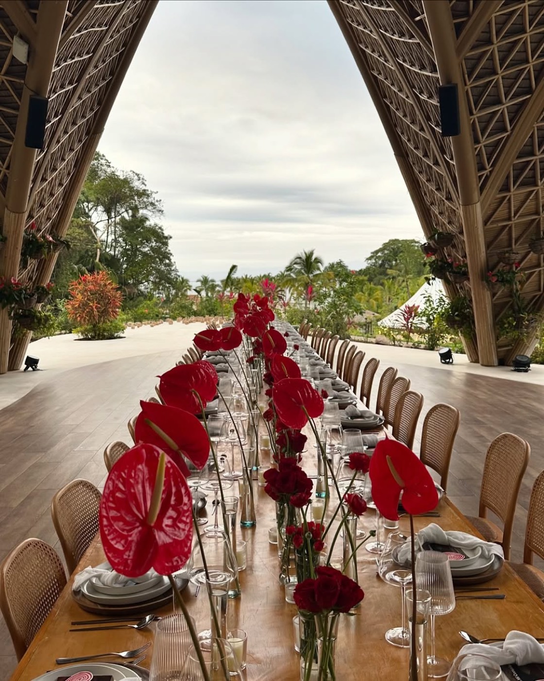 Mesa larga con anturios rojos bajo palapa de bambú